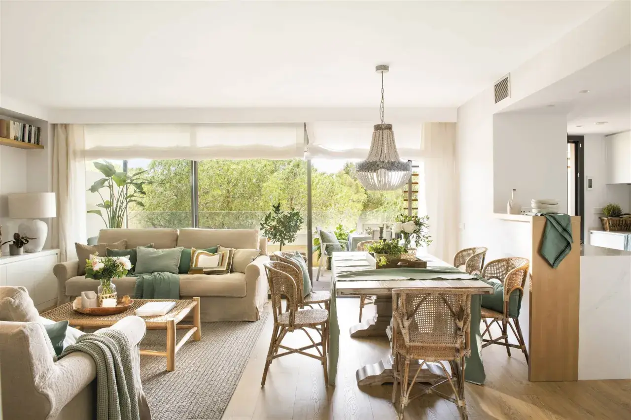Elegante decoracion salon con sofás, mesa de comedor de madera, sillas de mimbre y gran ventanal con vistas al exterior.