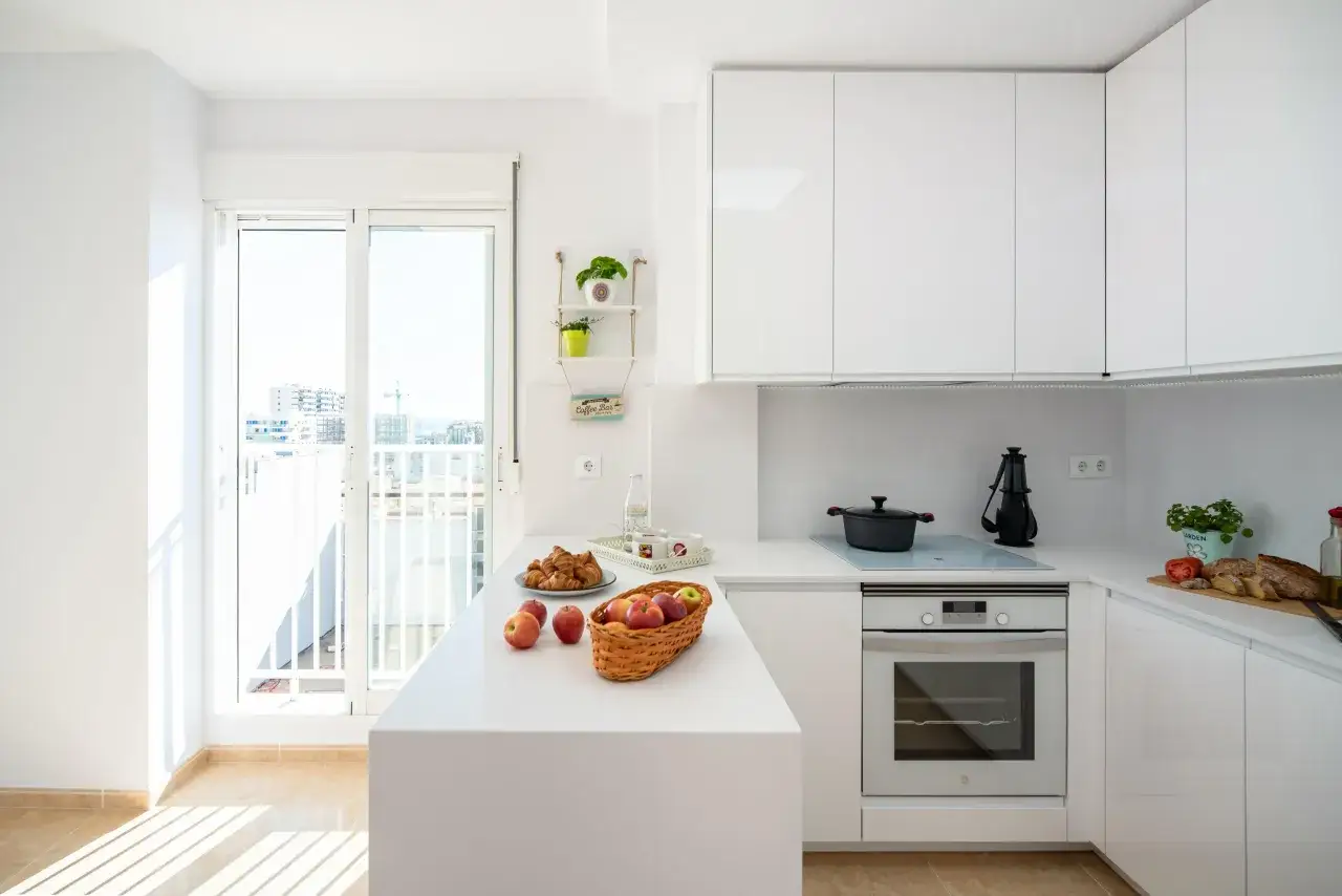 Cocinas pequeñas con barra, luminosas y modernas, con encimera blanca, electrodomésticos integrados y un balcón con vistas.