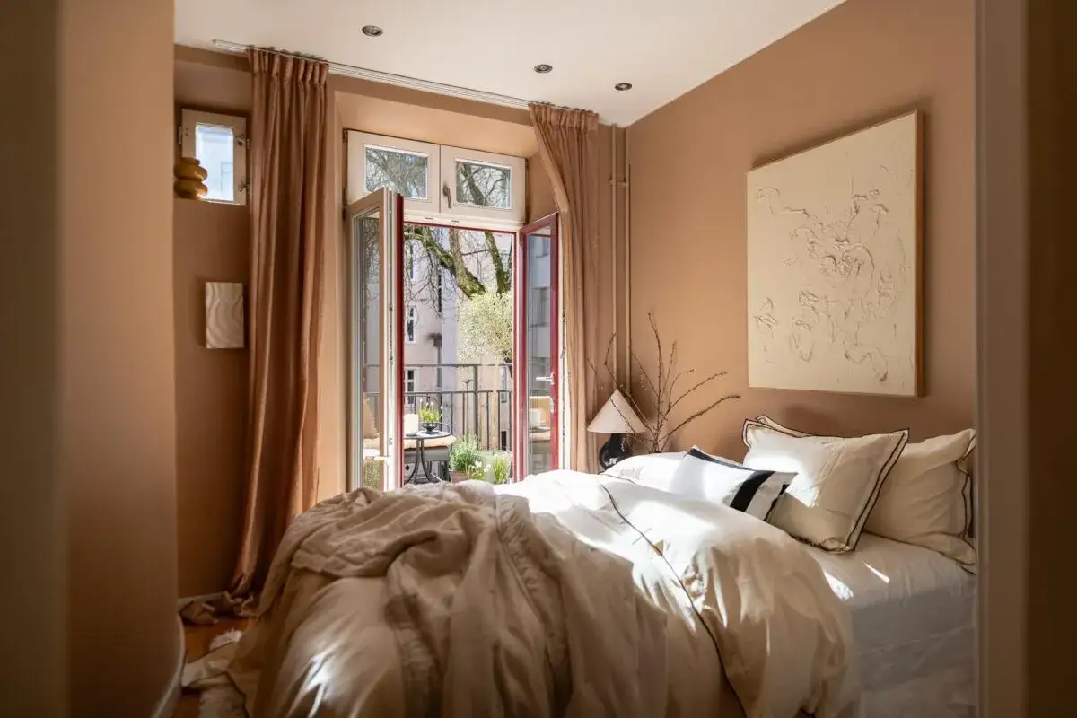 Acogedor dormitorio con paredes color terracota, cama vestida con funda nordica terracota y balcón abierto.