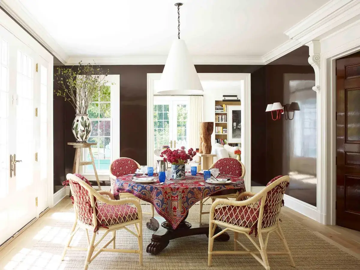 Comedor moderno con mantel estampado, sillas de mimbre y cojines rojos. Inspiración de colores para un espacio acogedor.