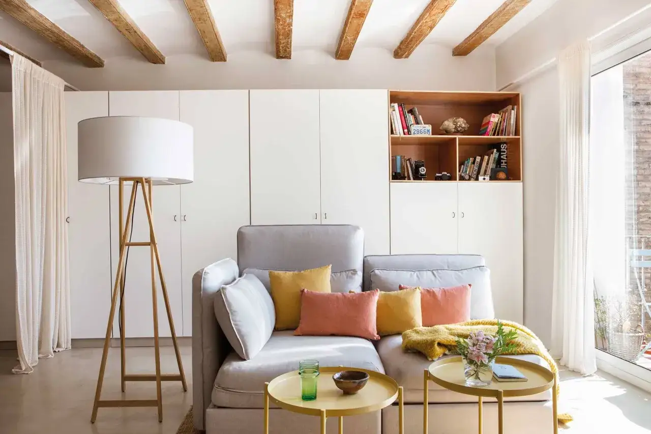 Salón acogedor con sofá gris, cojines coloridos y estantería de madera. Ideal para amueblar piso de alquiler con estilo y calidez.