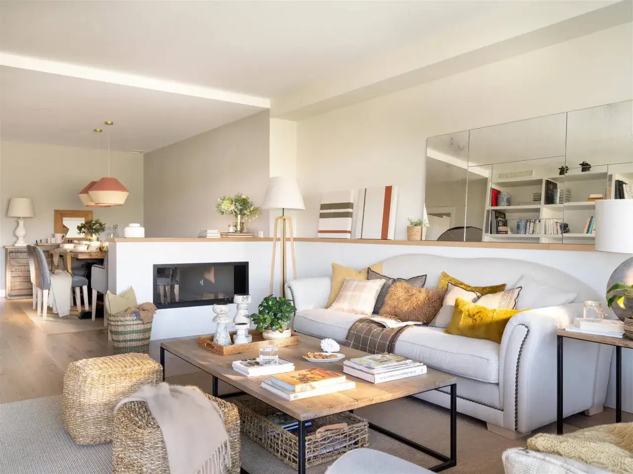 Ideas para amueblar salón rectangular: sofá blanco, mesa de centro de madera, pufs de mimbre, chimenea y estanterías con espejos.