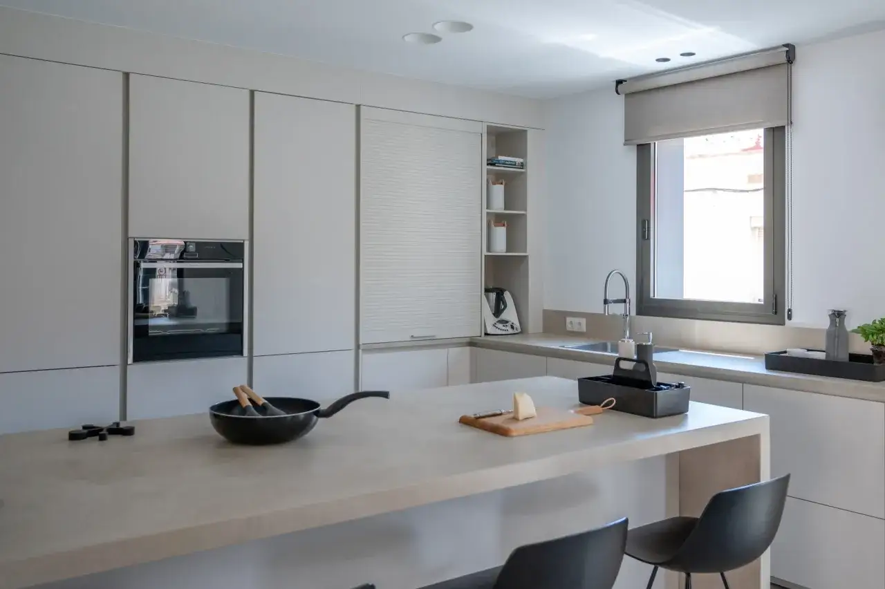 Cocina moderna con pen&iacute;nsula abierta al sal&oacute;n. Encimera de hormig&oacute;n, electrodom&eacute;sticos integrados y mobiliario minimalista.