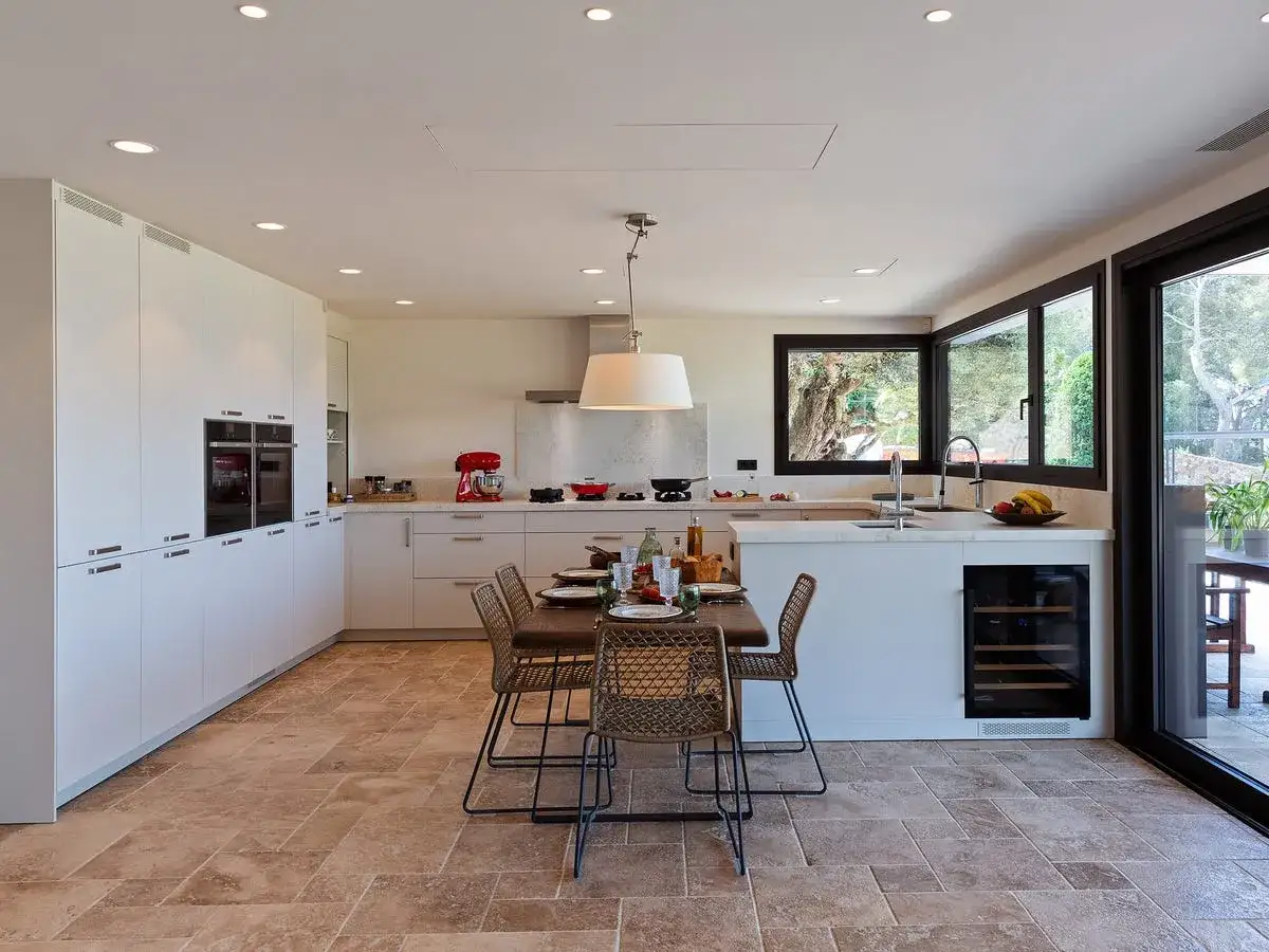 Moderna cocina americana y salón con isla central, electrodomésticos integrados y mesa de comedor. Ventanales con vistas al exterior.
