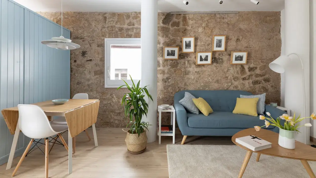 Un salón acogedor con paredes de piedra, un sofá azul y una mesa de comedor plegable. Un ejemplo de tiny living con estilo y funcionalidad.