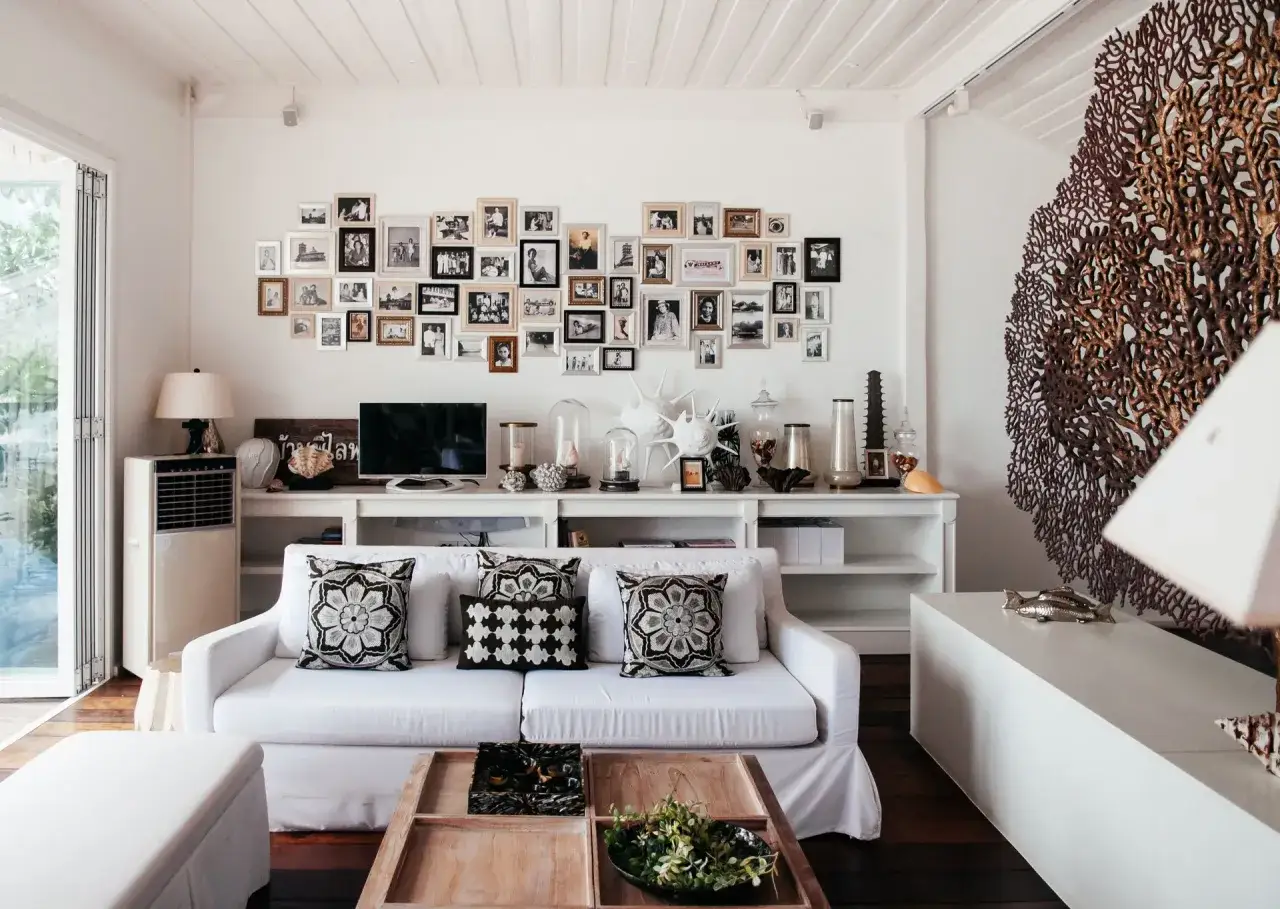 Sof&aacute; blanco con cojines decorativos, mesa de centro de madera y pared adornada con fotos. Una reforma sin obras que transforma el espacio con estilo.