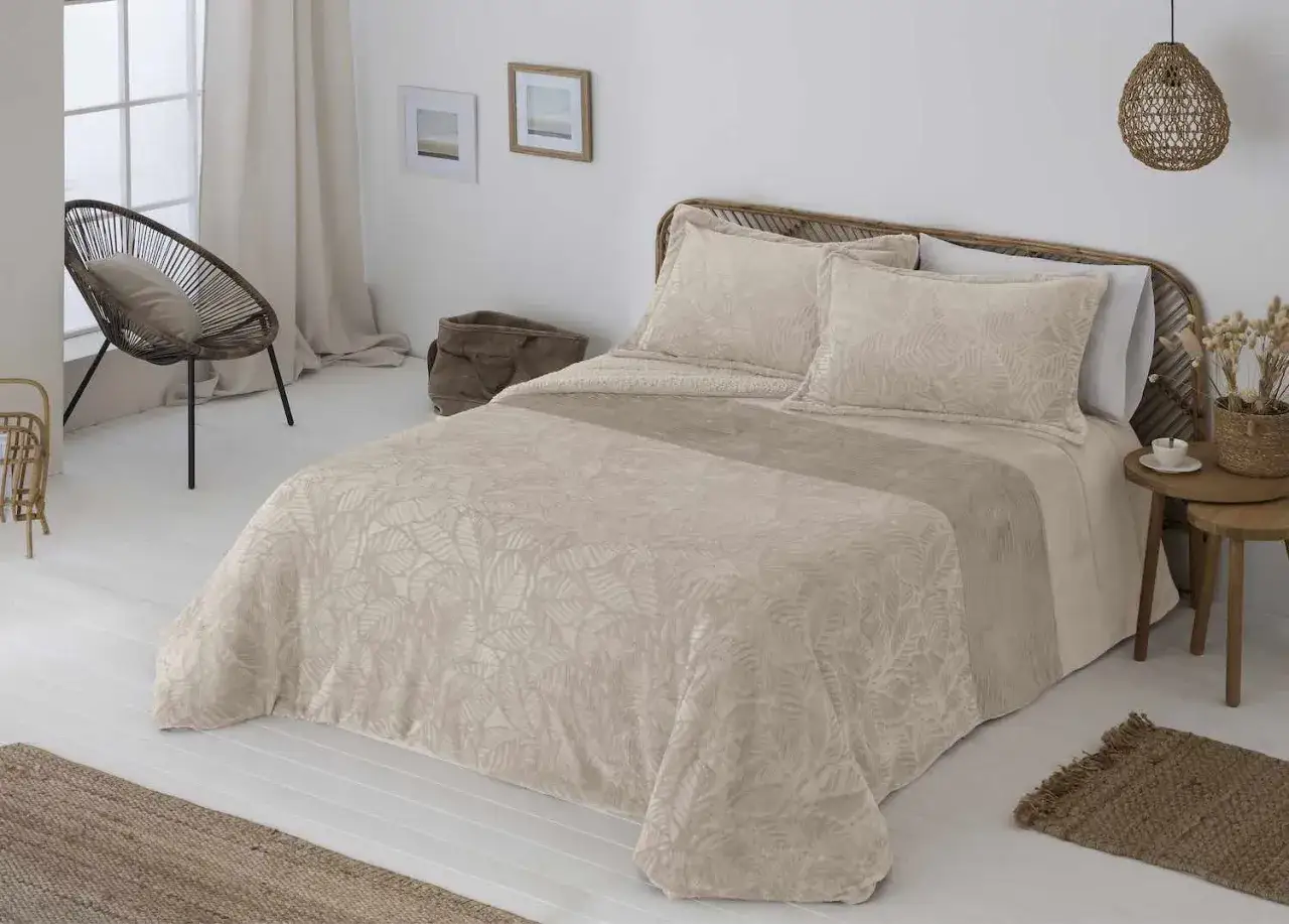 Edredón antilo con estampado de hojas en tonos beige, sobre una cama con cabecero de mimbre.