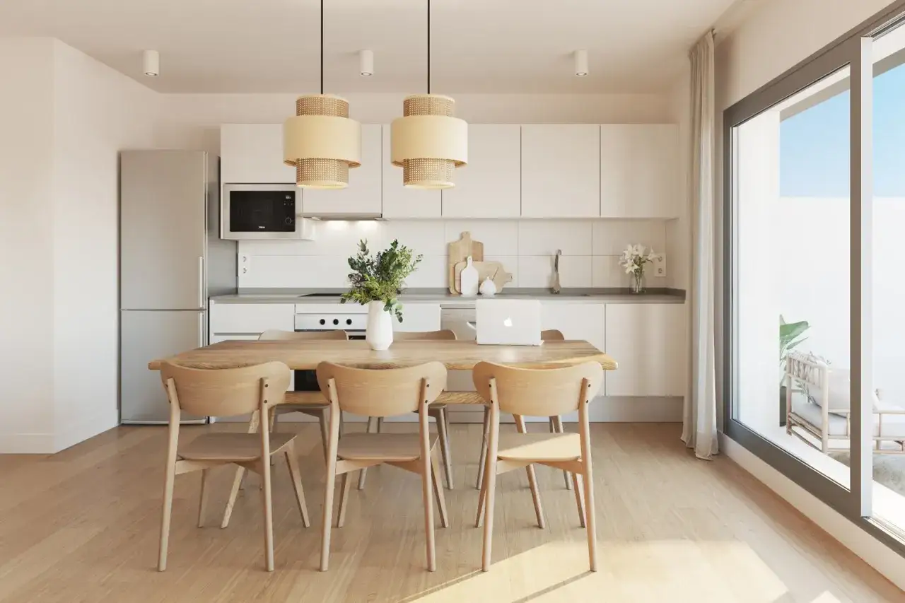 Comedor y cocina luminosos con muebles de madera clara y electrodomésticos blancos. El espacio irradia una sensación de calma y amplitud gracias a sus colores claros.