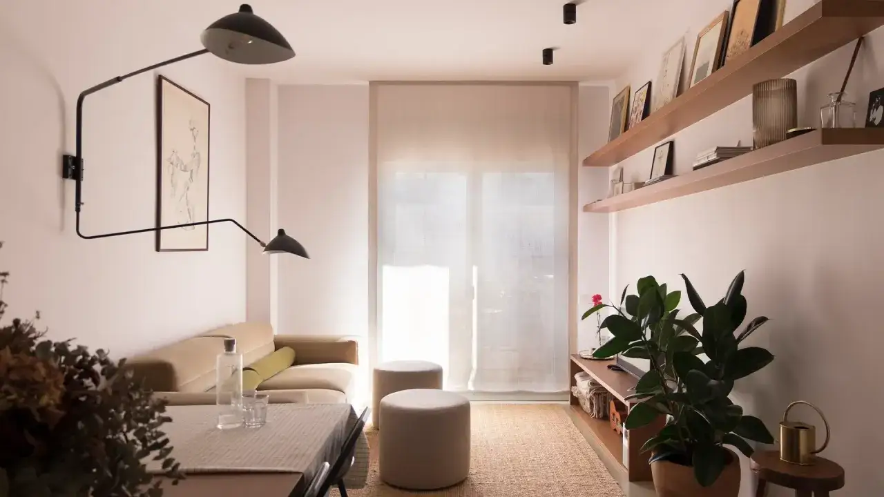 Salón moderno con sofá beige, mesa de comedor y suelos microcemento interior. Estanterías flotantes con decoración y plantas.