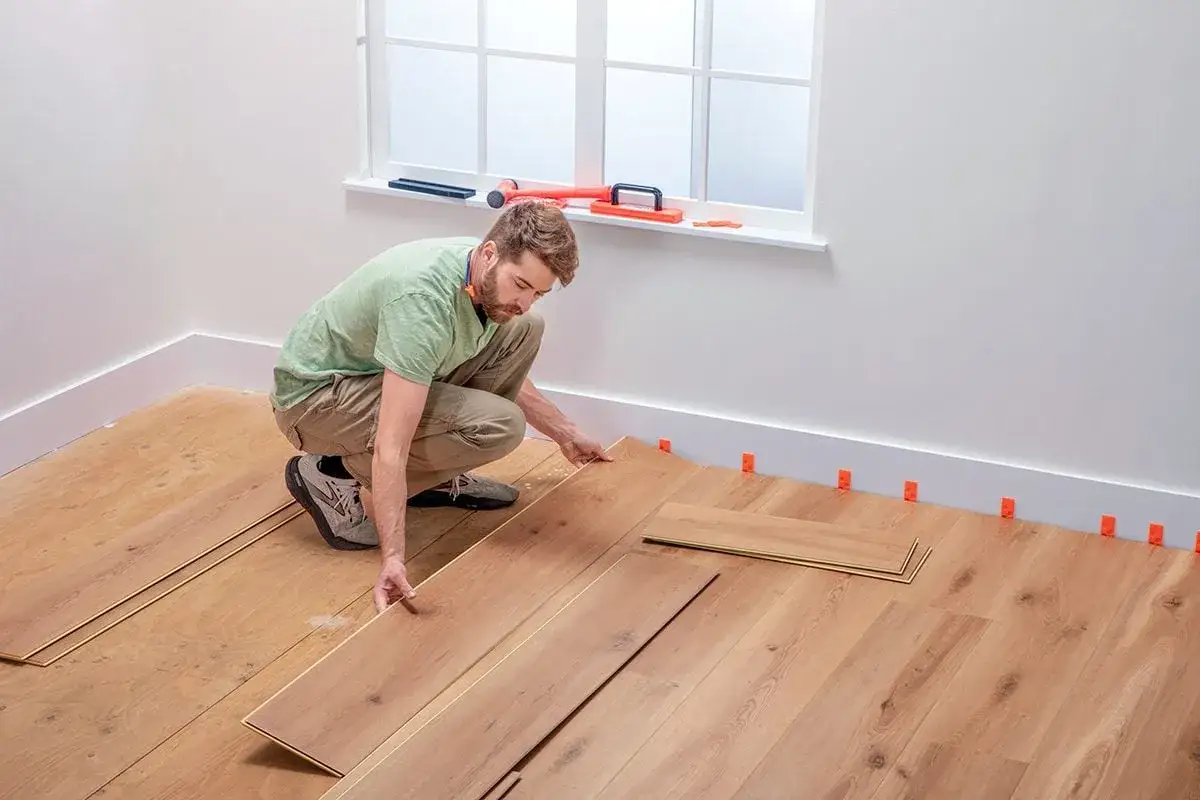 Hombre instalando tablas de madera para poner suelo vinílico. Se ven cuñas naranjas en el zócalo.