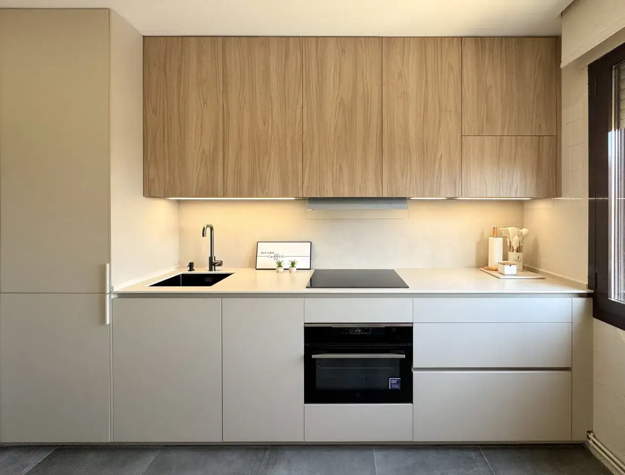 Cocina moderna con gabinetes de madera y blanco, encimera clara, fregadero negro y horno empotrado. Una clara tendencia en cocinas minimalistas.
