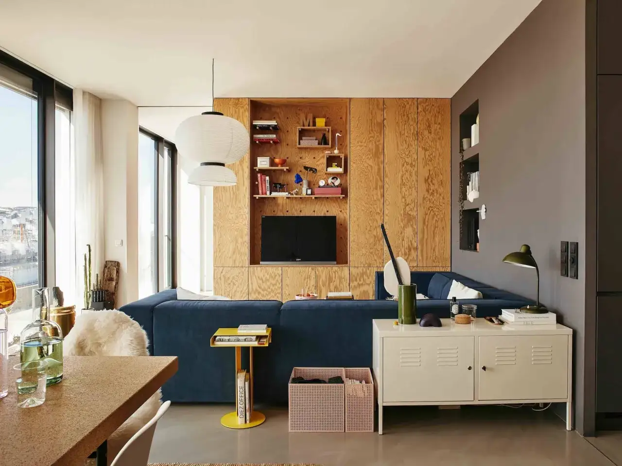 Un salón moderno con sofá azul, estanterías de madera y lámparas colgantes. Un espacio acogedor para tini living.