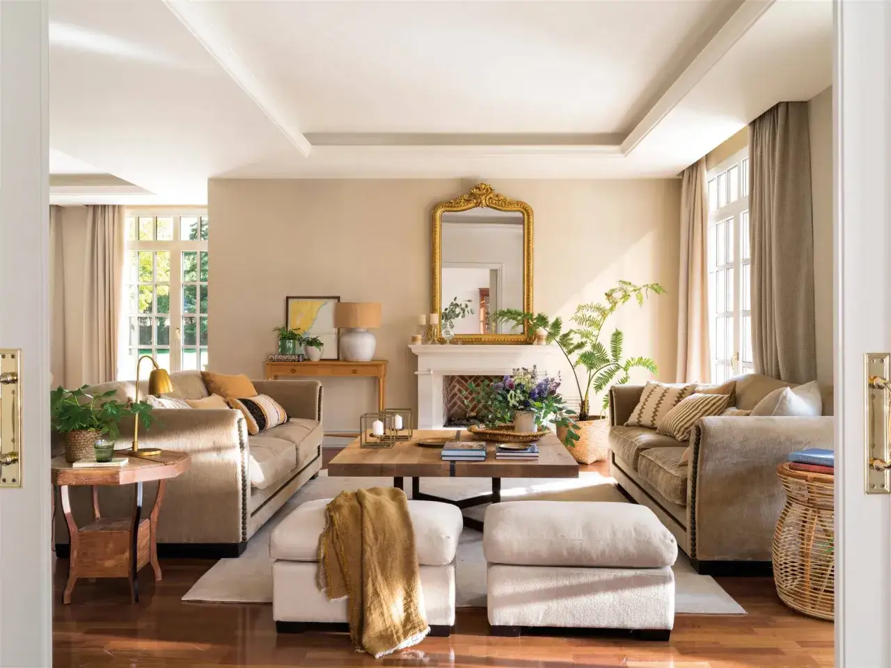 Elegante sal&oacute;n con sof&aacute;s beige, mesa de centro de madera y chimenea. Diversos estilos de decoraci&oacute;n se combinan para crear un ambiente acogedor.