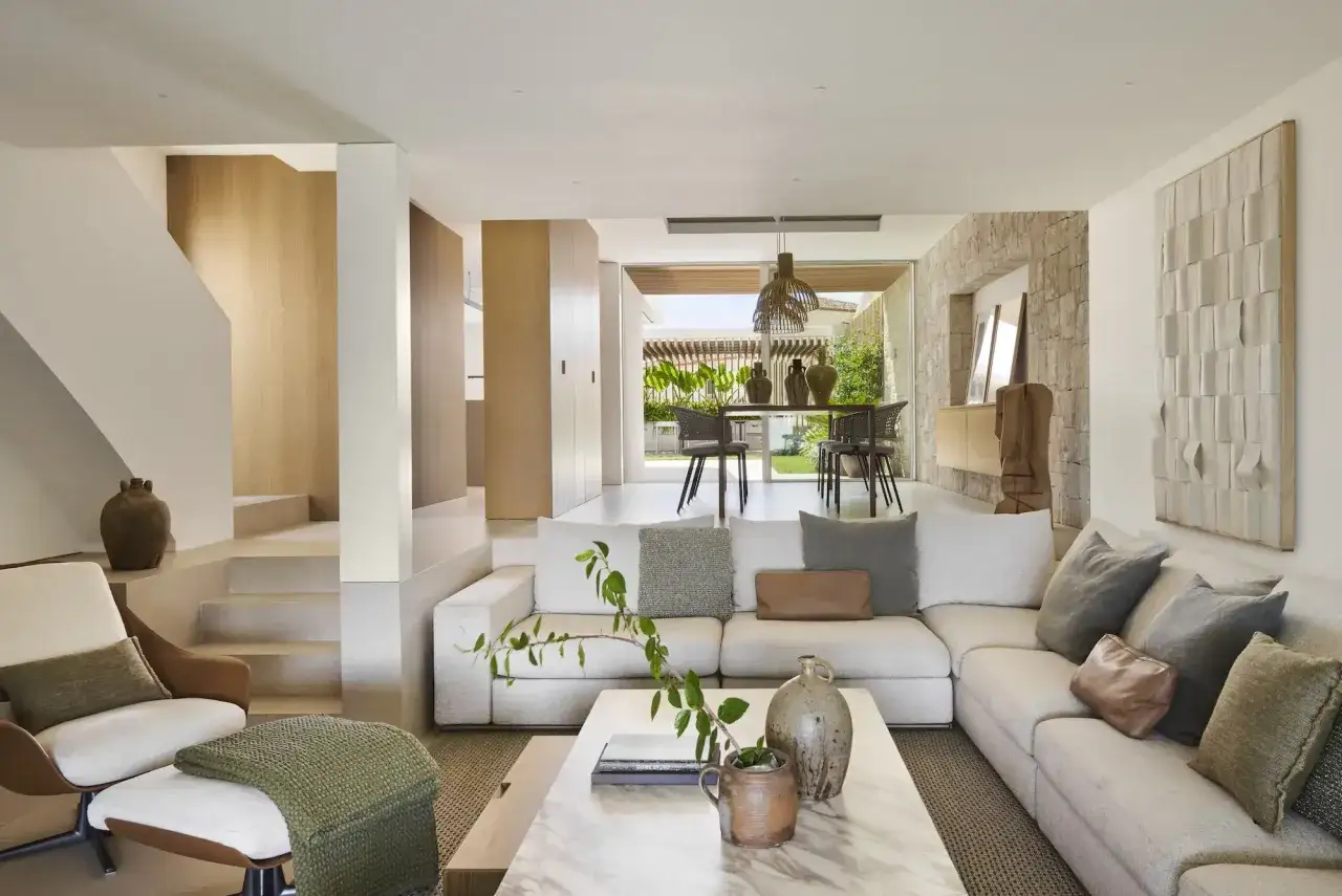 Amplio salón comedor alargado con sofá modular, escaleras de madera y vistas al jardín.