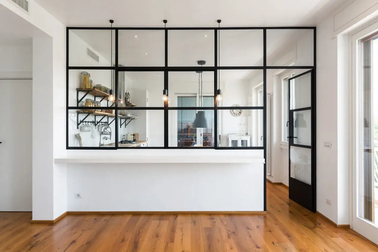Moderna separación pared cristal cocina salón con estanterías y lámparas colgantes.