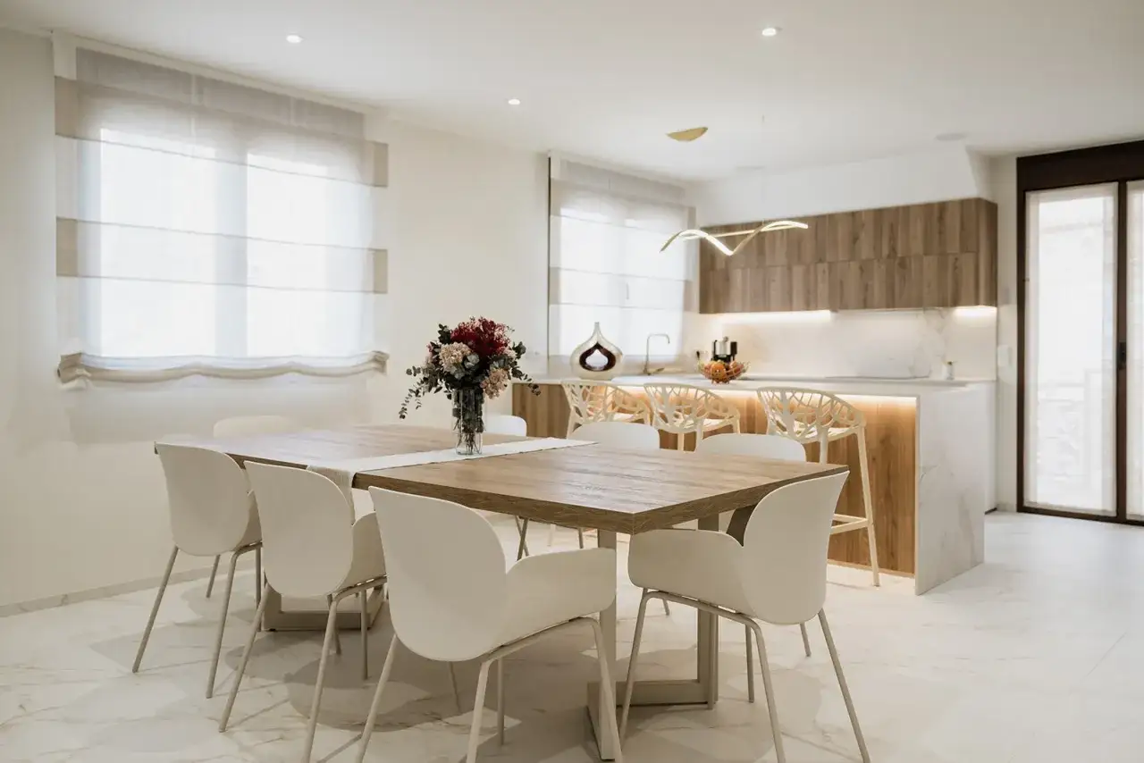 Elegantes cocinas abiertas al salón con barra, mesa de comedor y sillas blancas, creando un espacio moderno y luminoso.