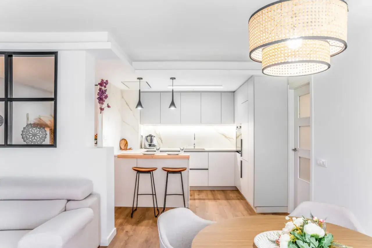 Un moderno salón cocina pequeño con isla, taburetes de madera y un sofá gris.