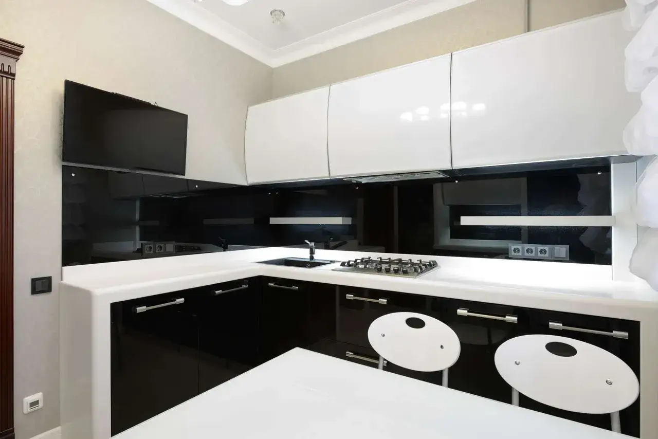 Elegantes cocinas en blanco y negro con gabinetes brillantes, encimeras blancas y un televisor de pantalla plana.