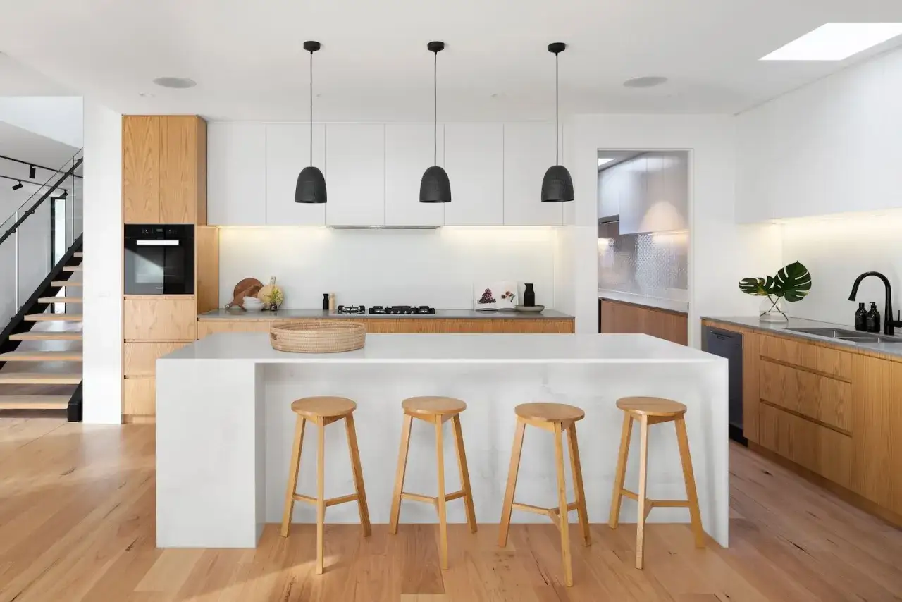 Ideas para como diseñar una cocina moderna: isla blanca, taburetes de madera, gabinetes de roble y luces colgantes negras.