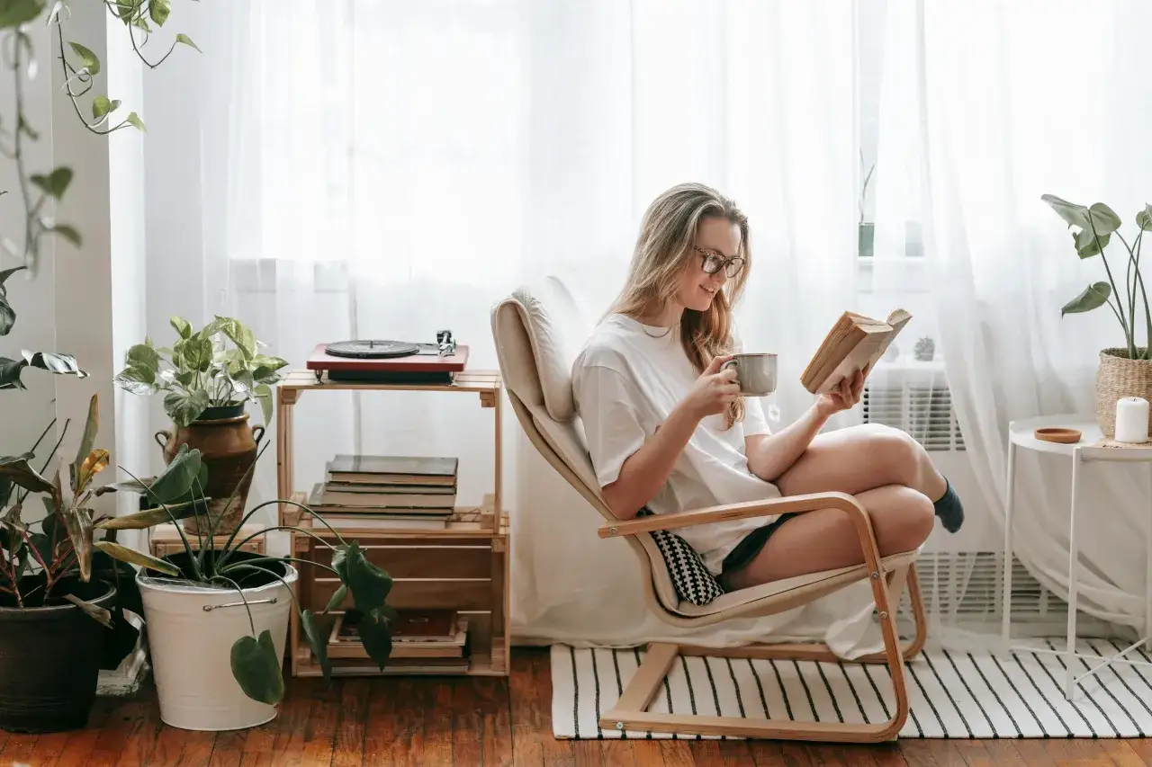 Mujer leyendo un libro en un acogedor rinc&oacute;n lectura sal&oacute;n, con plantas y una taza de t&eacute;.