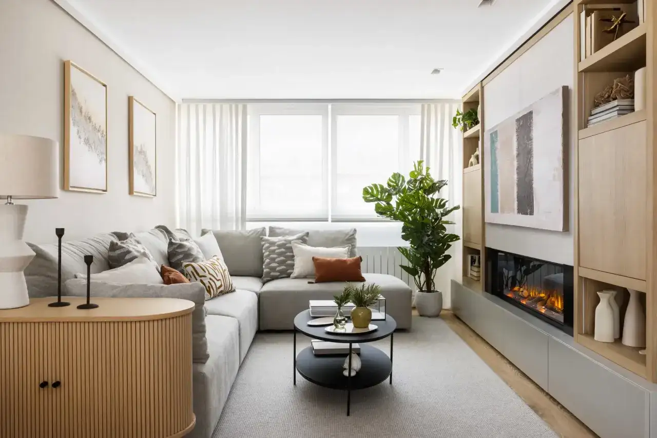Elegante decoracion salon pequeño con sofá gris, chimenea moderna, planta y muebles de madera.