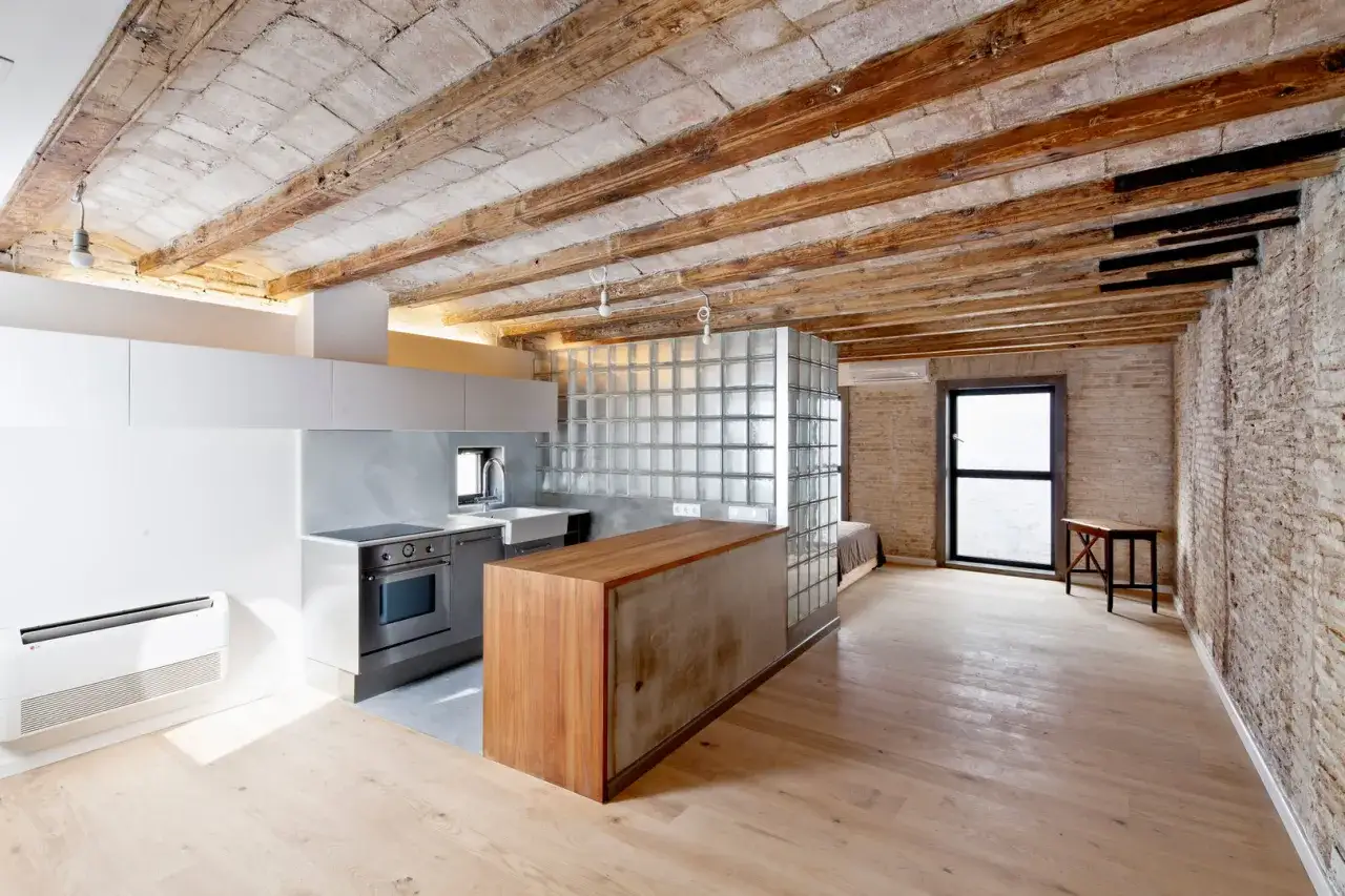 Cocina moderna con isla de madera y cristal, techos de vigas expuestas. Imagina como tirar un tabique para crear este espacio abierto.