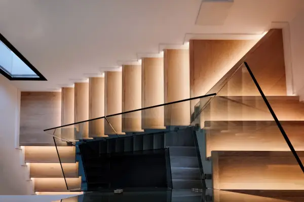 Moderna escalera de madera con iluminación indirecta y barandillas de cristal, vistas en el salón.