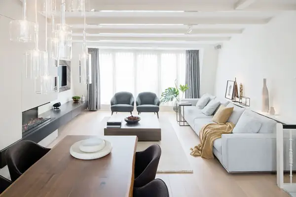 Elegante decoracion salon comedor con chimenea, sofá gris, mesa de madera y sillas oscuras.