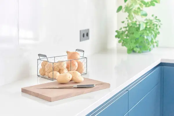 Encimeras de cocina blancas y lisas, con patatas y cebollas listas para cocinar.