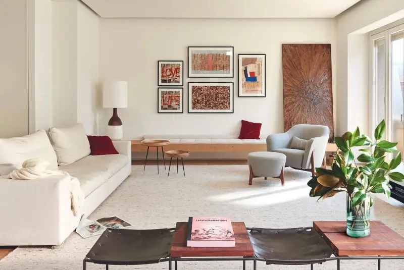 Una composición de cuadros en la pared, con arte abstracto y tipografía, decora este salón moderno junto a un sofá blanco y una butaca gris.